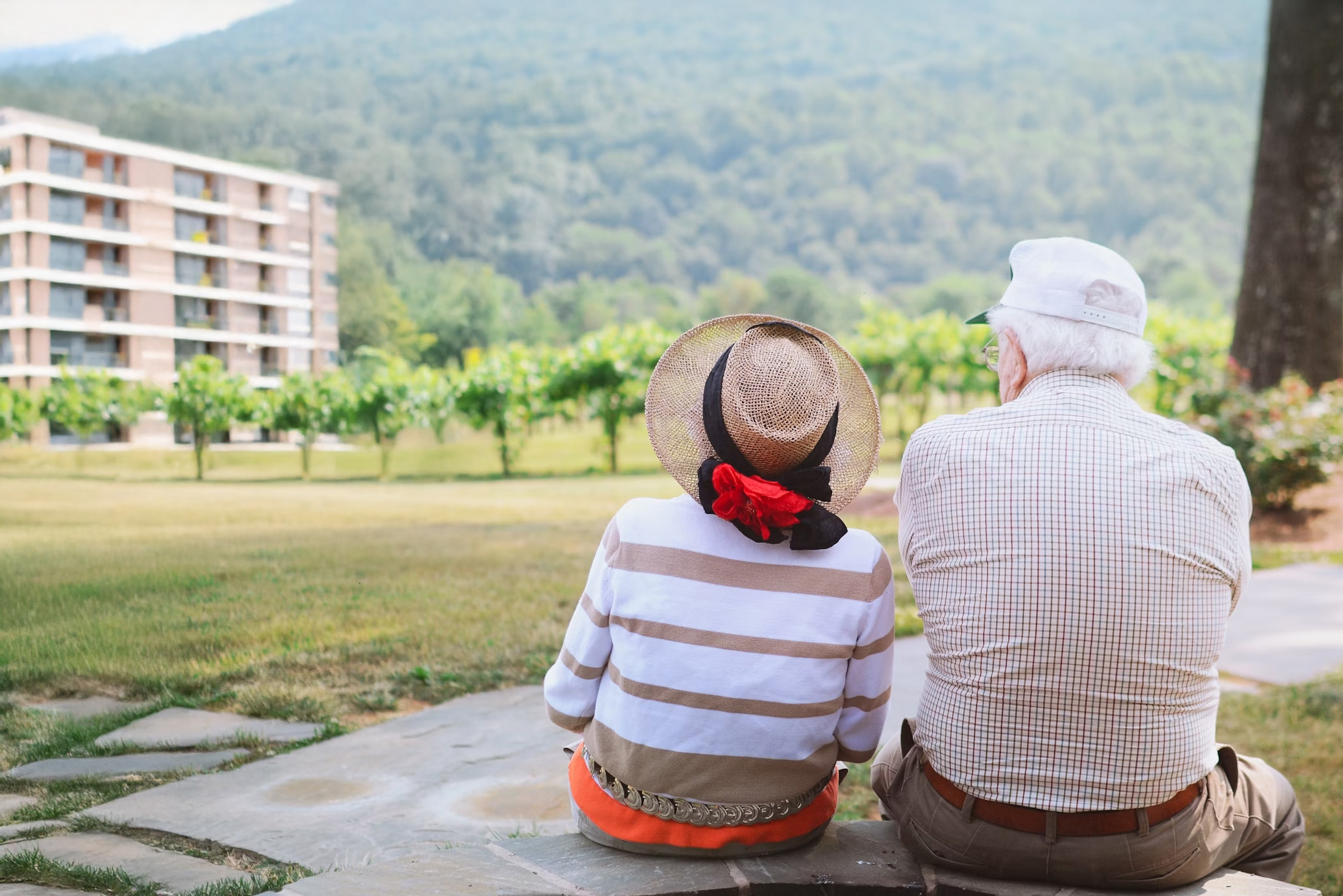 Äldre kvinna och man sitter på en stenbänk och ser fram emot boende i ett flerfamiljshus